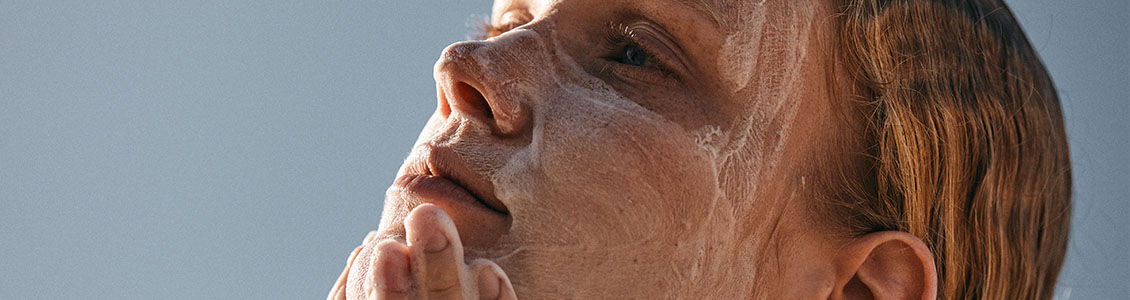 The image shows the face of a woman looking up  massaging her face with a cleanser