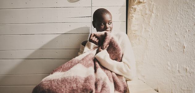 The image shows a woman sitting down wrapping herself with a blanket