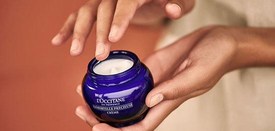 The image shows the hands of a person about to take out some of the L'OCCITANE Immortelle precious Cream