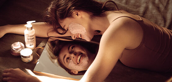 Woman looking in mirror in order to apply L'OCCITANE Soothing Face Mask to face.