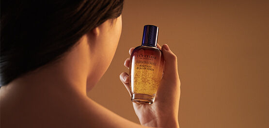 The image shows a woman looking directly at the L'OCCITANE Immortelle Reset Serum