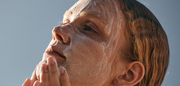 The image shows the face of a woman looking up  massaging her face with a cleanser