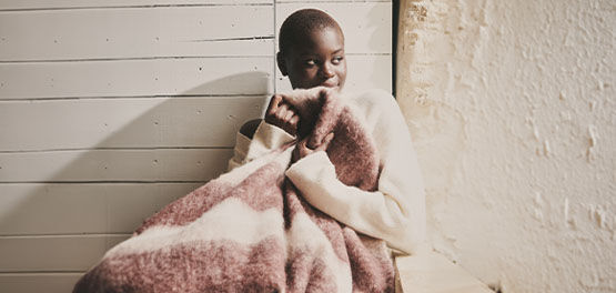 The image shows a woman sitting down wrapping herself with a blanket