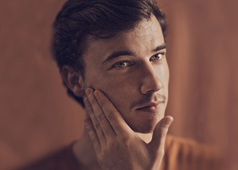 The image shows a man gently touching his face