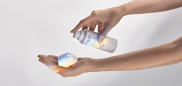 A close-up image showing the hands of a person applying the L'OCCITANE Reine Blanche Intense Illuminating Foam