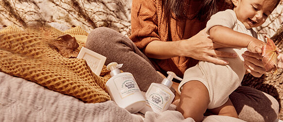 Mother holding baby, using L'OCCITANE Shea Baby Cuddles & Bubbles Foaming Cream, Shea Baby Lovely & Gentle Moisturising Milk & Bonne M&egrave;re Extra Pure Soap